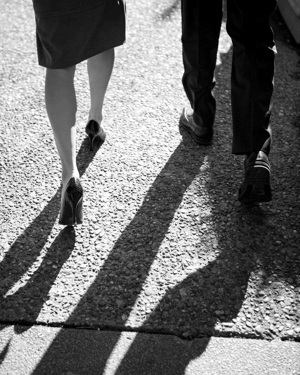 Two people walking with long shadows on the pavement