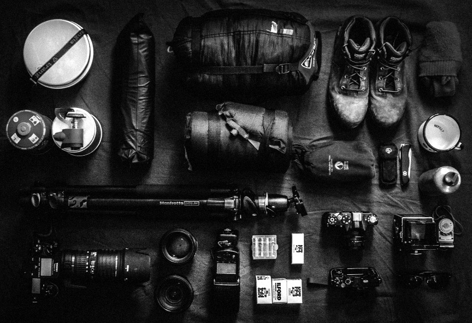 Cameras, lenses, film and travel gear laid out on a dark floor